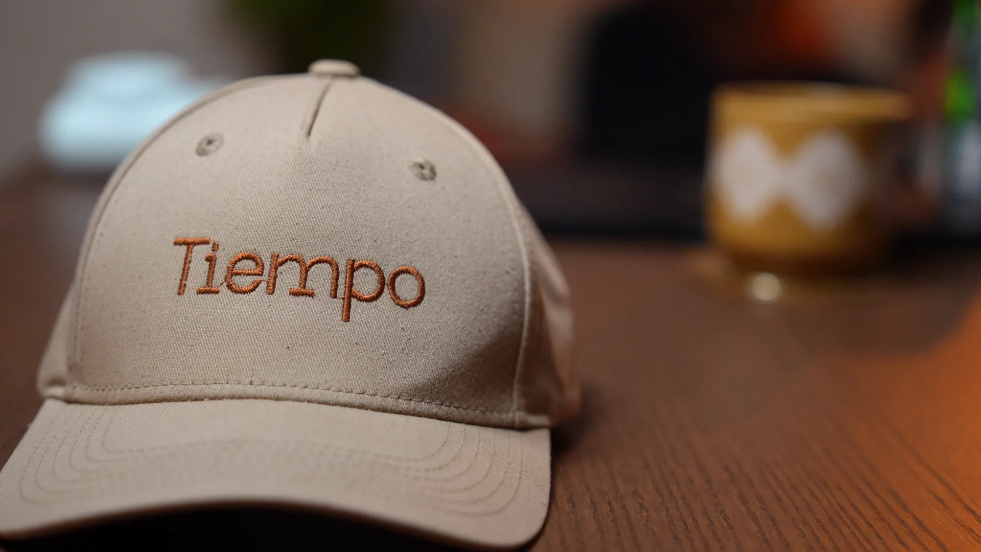 A tan Tiempo cap on a warm wood desk in soft morning light, with a coffee mug in the background