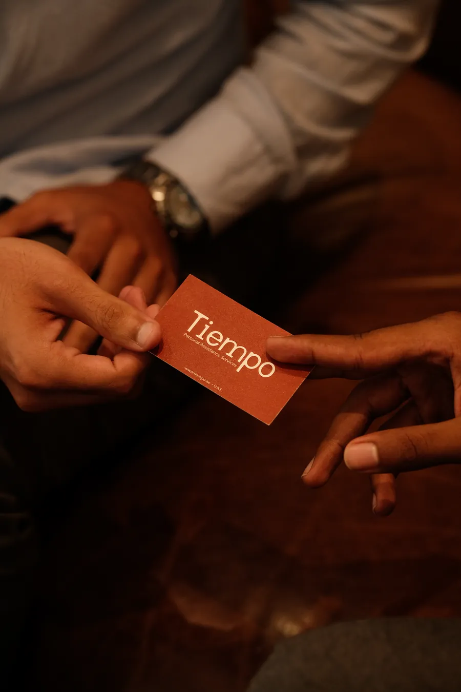 A Tiempo business card passing from one person's hand to another