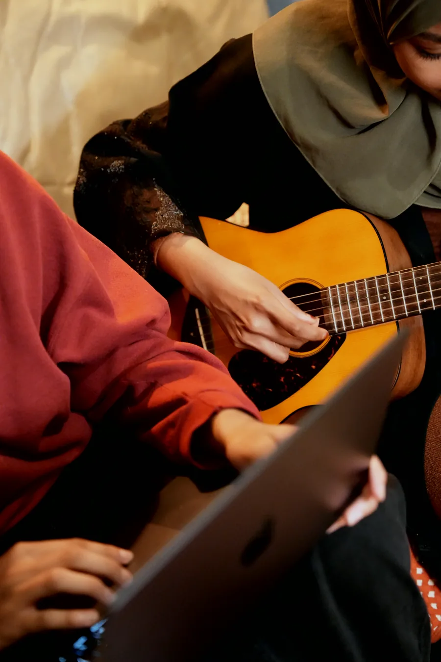 Two Tiempo team members relaxing together, one playing acoustic guitar and one on a laptop