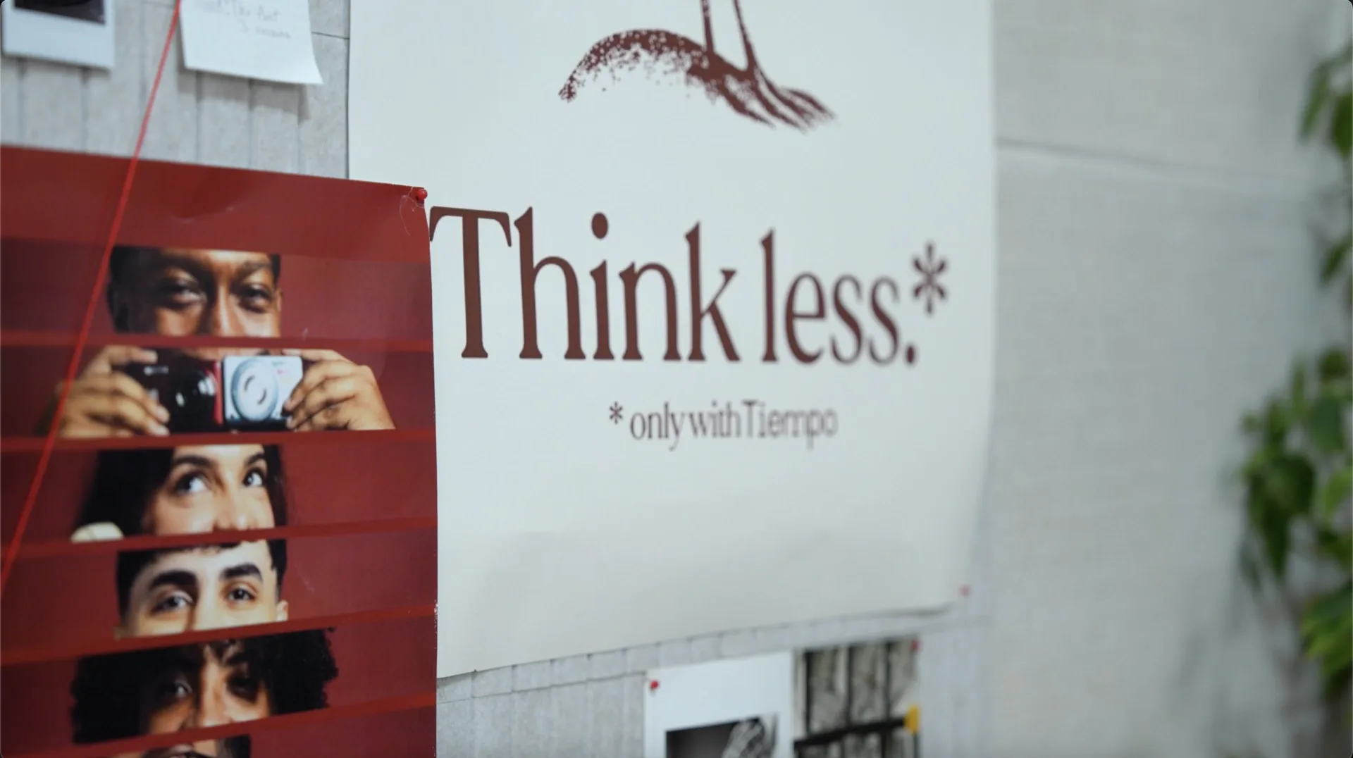 A Tiempo brand poster on a studio wall reading Think less, only with Tiempo, next to a multi-portrait collage